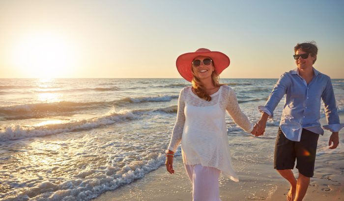 Morning, couple and walking in beach, outdoor and happiness for vacation, holding hands and holiday in Florida. Trip, man and woman in honeymoon, pregnant and bonding in sea, date or together on sand.